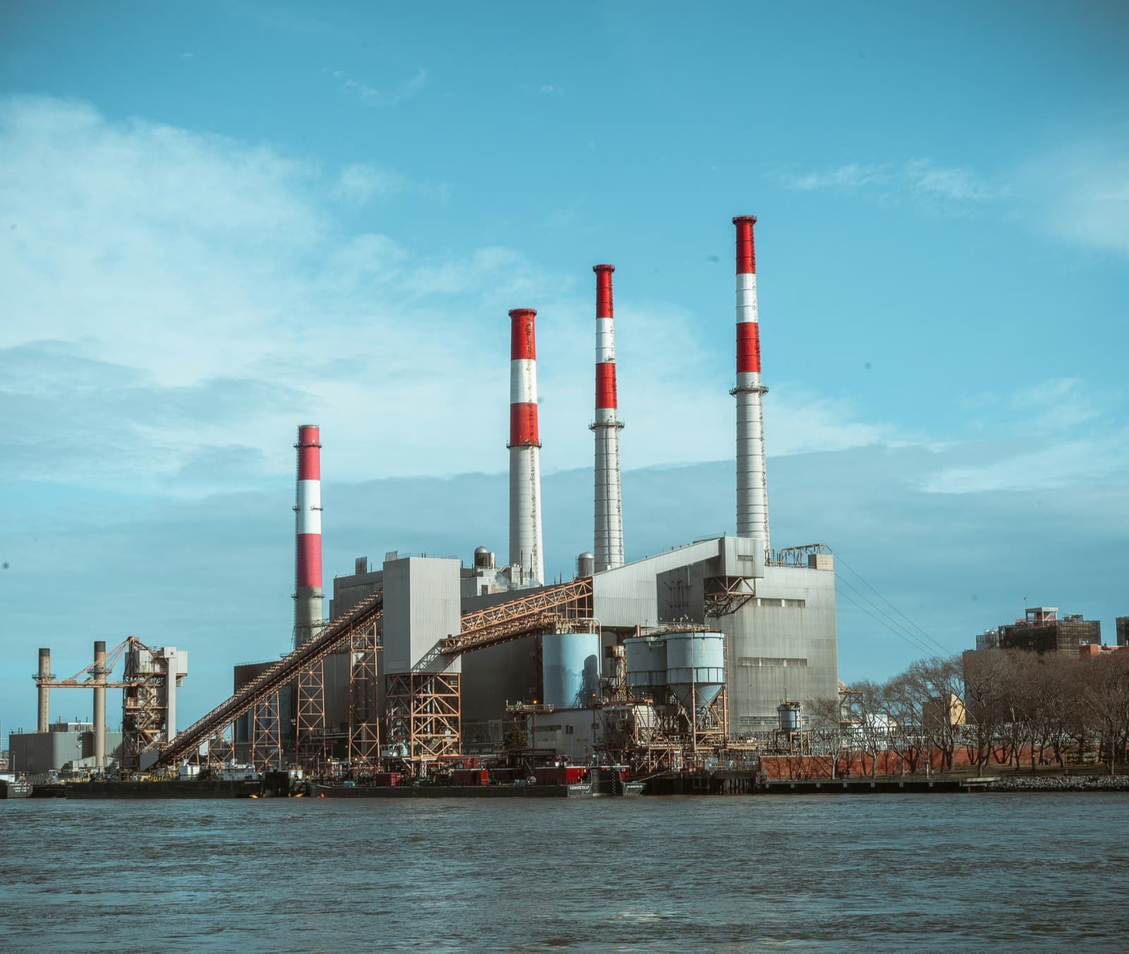 A riverside industrial plant with tall red-and-white banded chimneys.