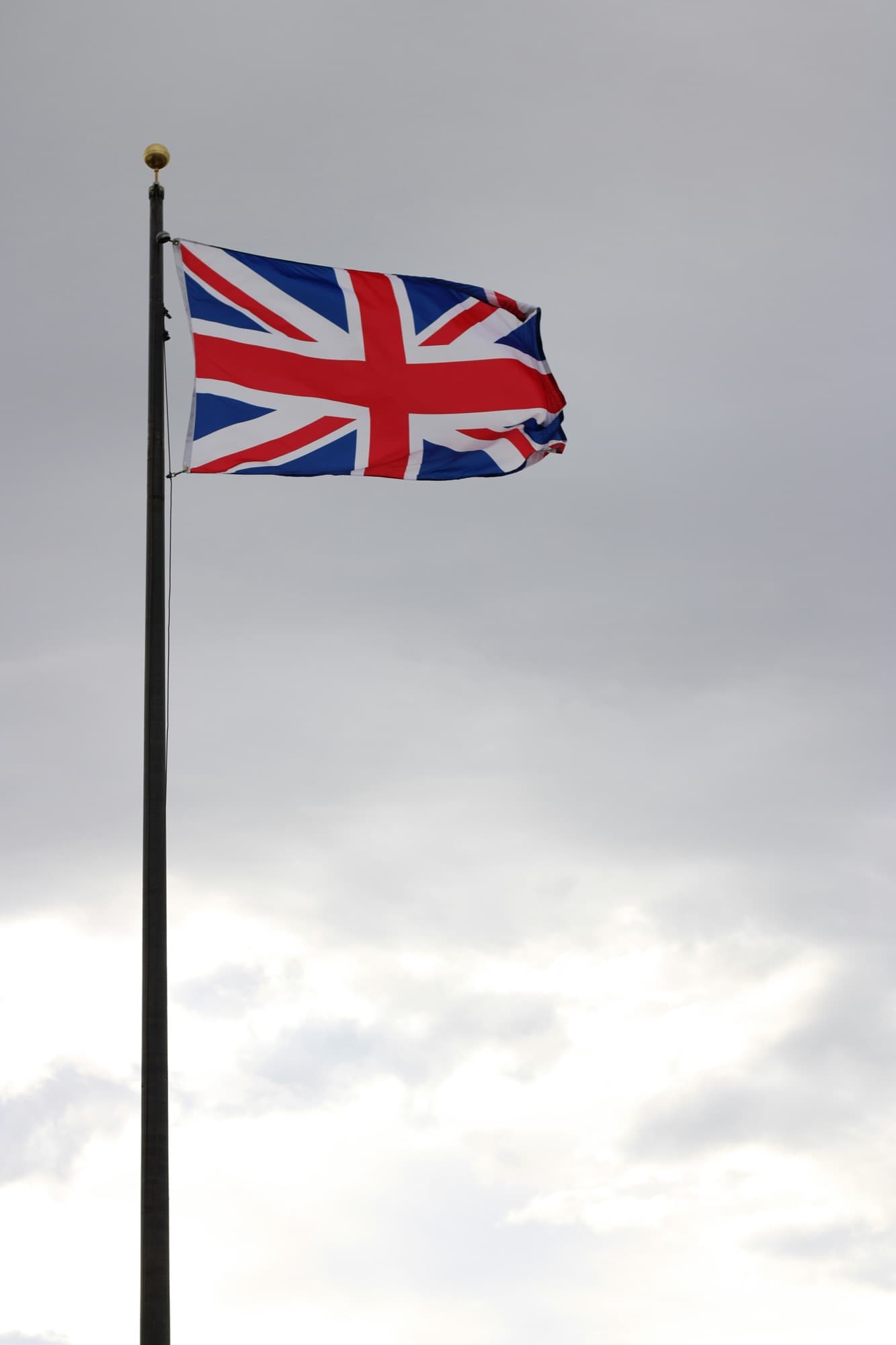 The Union flag flying from a tall mast against an overcast British sky.